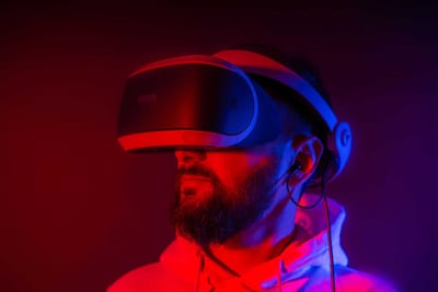 Man wearing a virtual reality headset, illuminated by red and blue lighting, looking upward.